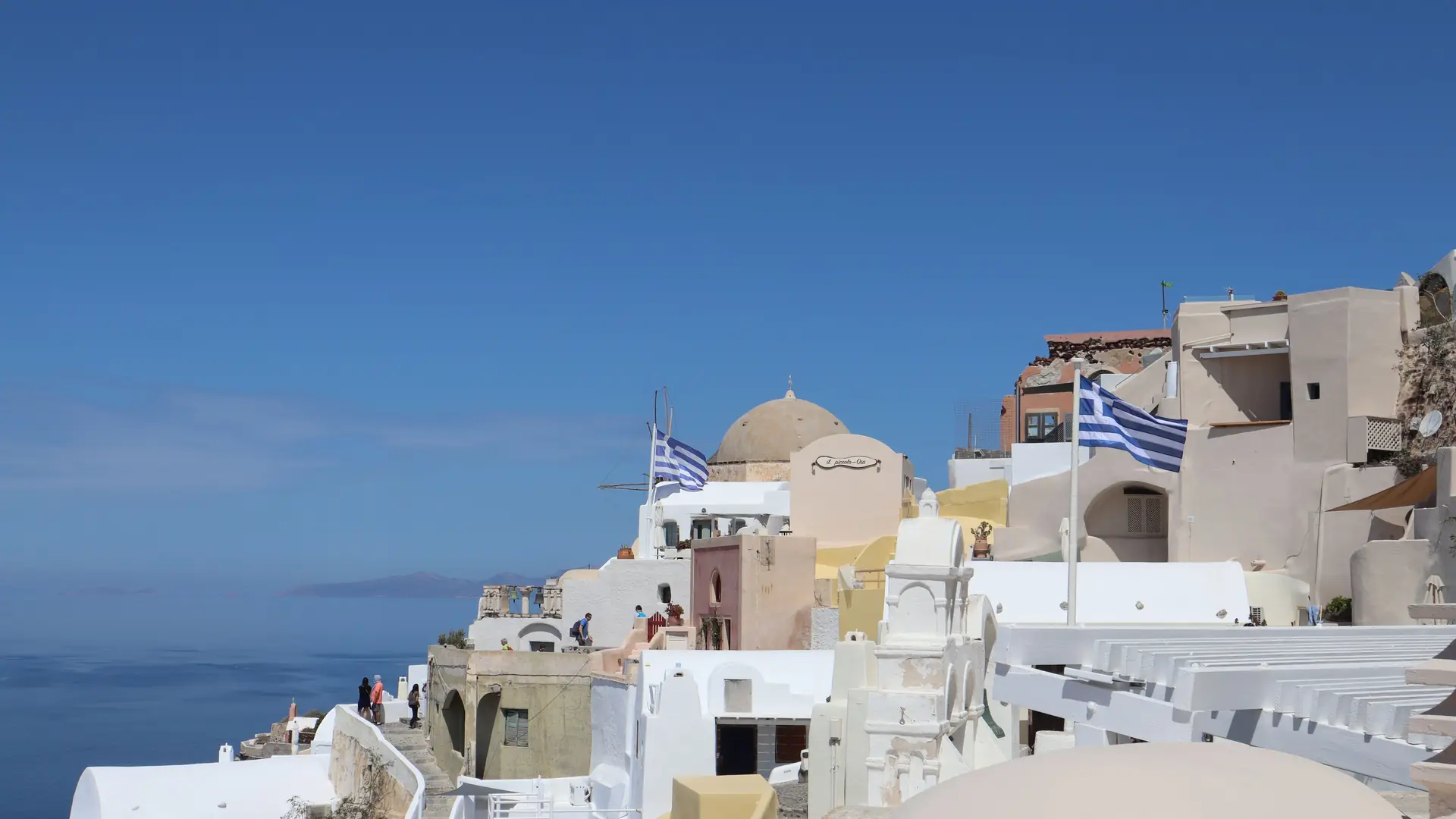 Churches and white houses on the cliff edge at Oia, Santorini, under a deep blue sky