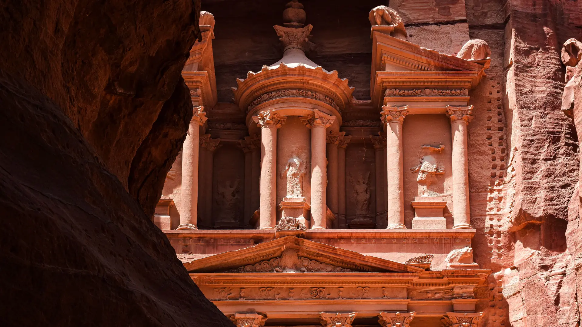 The rose-red columns of the Treasury at Petra, glimpsed past a dark canyon wall