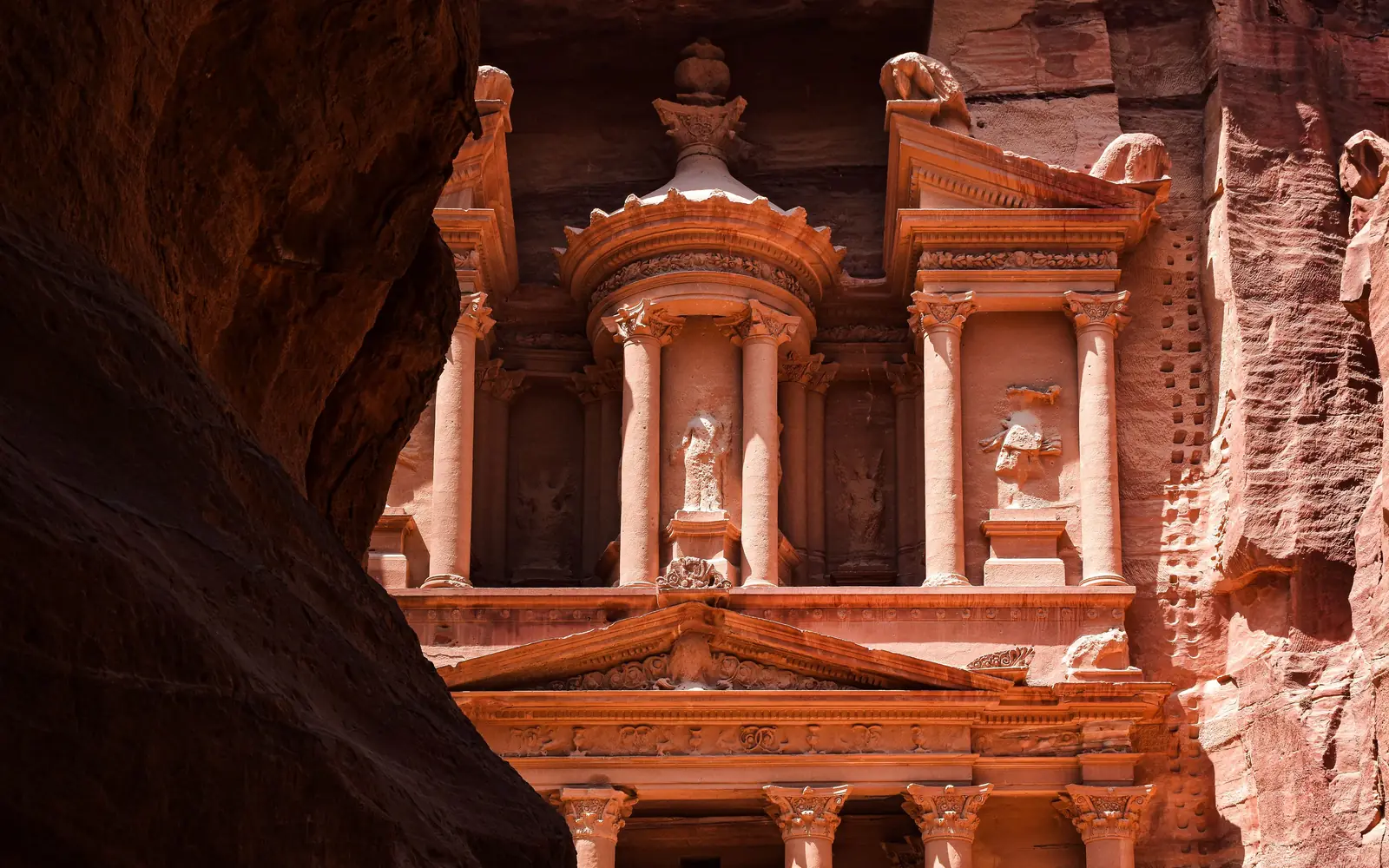 The rose-red columns of the Treasury at Petra, glimpsed past a dark canyon wall